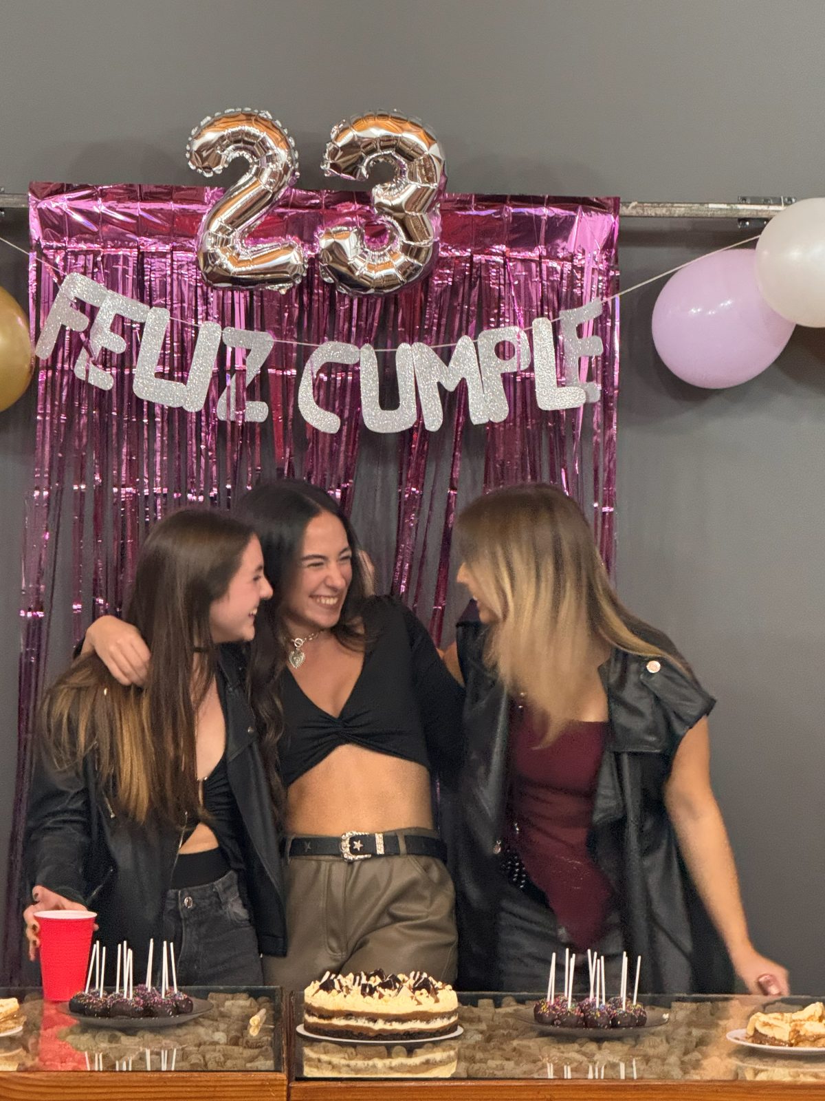 Tres amigas festejando un cumpleaños en el quincho, con globos y cortina metalizada