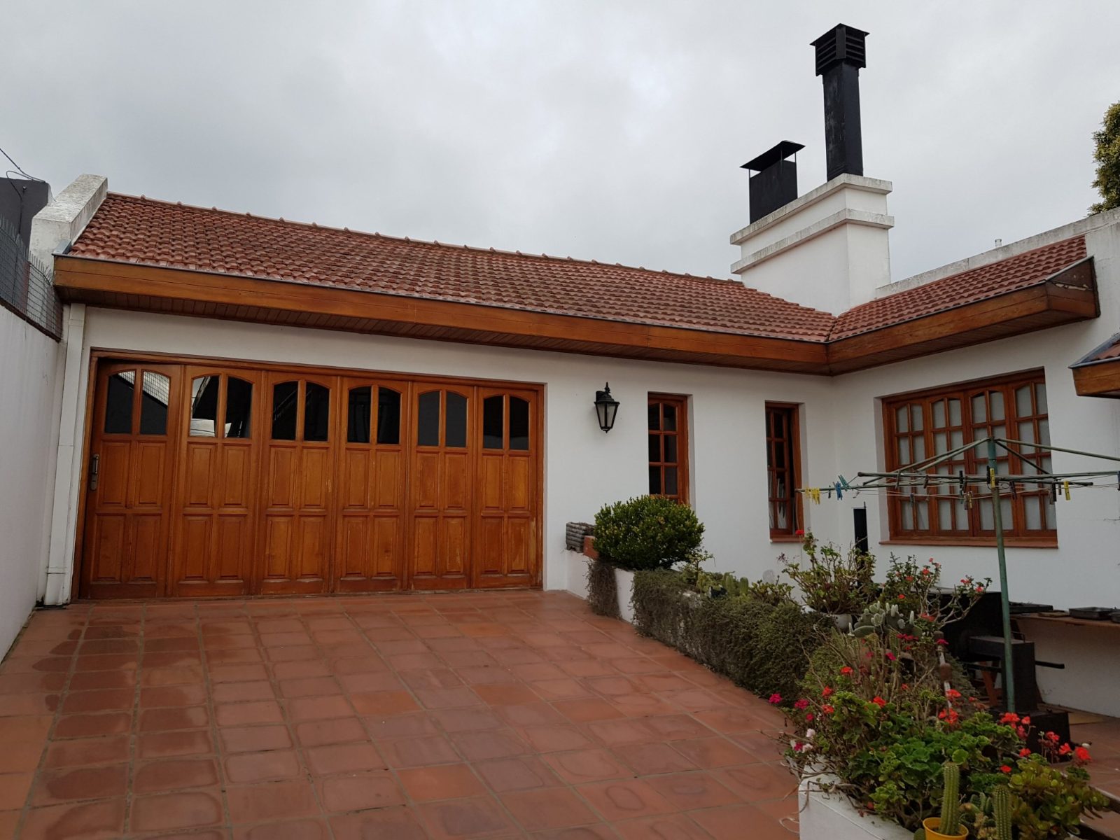 El frente del quincho: portón de madera, techo de tejas y patio de baldosas