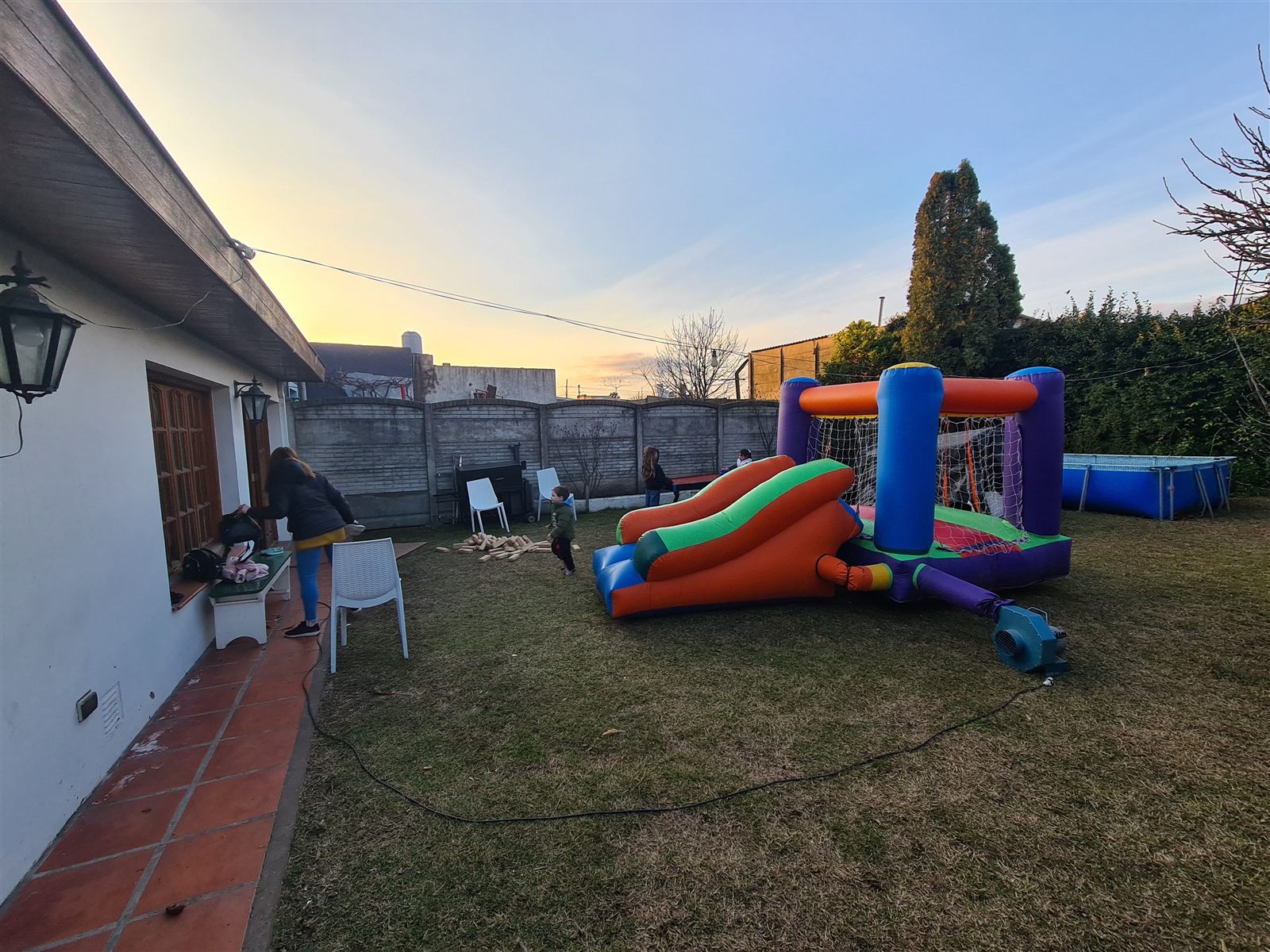 El patio al atardecer con un castillo inflable, juegos de madera y chicos jugando