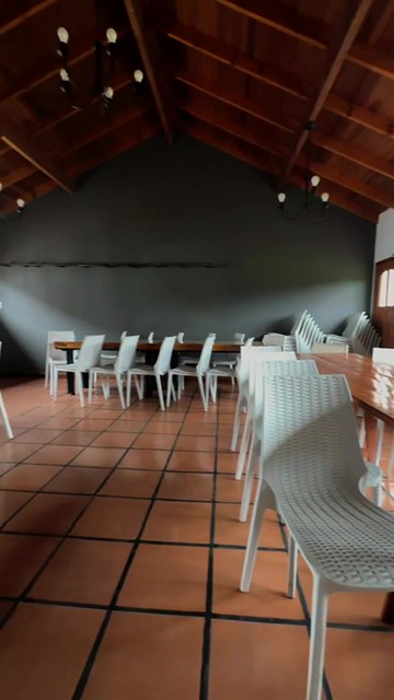 El salón con techo de madera, mesas largas y sillas blancas